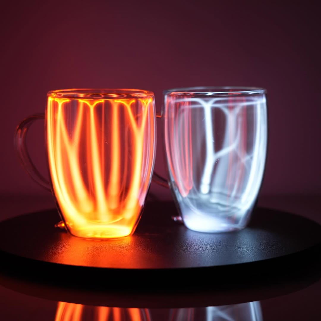 Two Plasma Mugs by Astro Labs glowing with blue and red plasma filaments inside a clear double-walled glass mug on a powered base.
