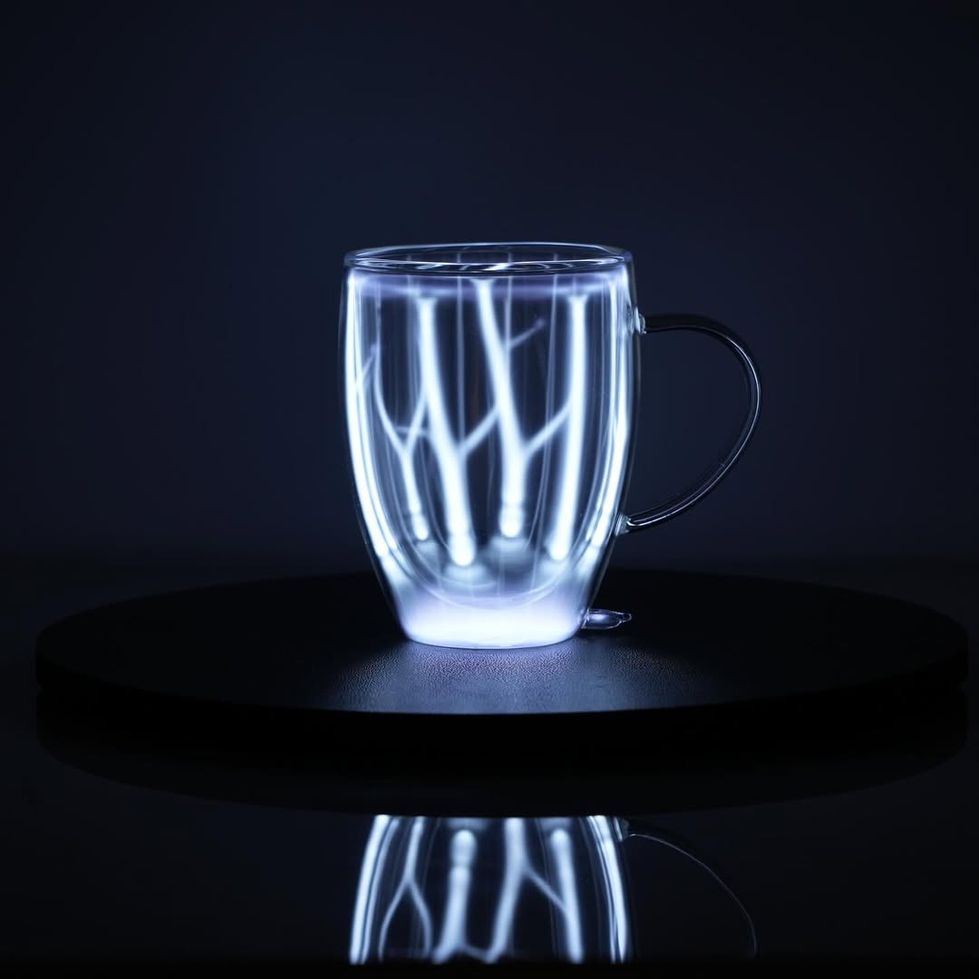 Plasma Mug by Astro Labs glowing with blue plasma filaments inside a clear double-walled glass mug on a powered base.
