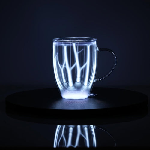 Plasma Mug by Astro Labs glowing with blue plasma filaments inside a clear double-walled glass mug on a powered base.