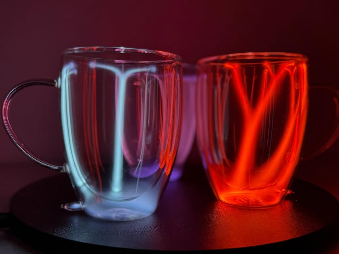 Two Plasma Mugs by Astro Labs glowing with blue and red plasma filaments inside a clear double-walled glass mug on a powered base.